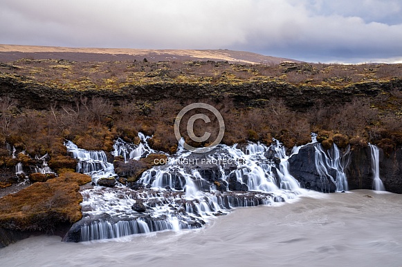 Hraunfossar waterfalls flowing into a dark, turbulent river